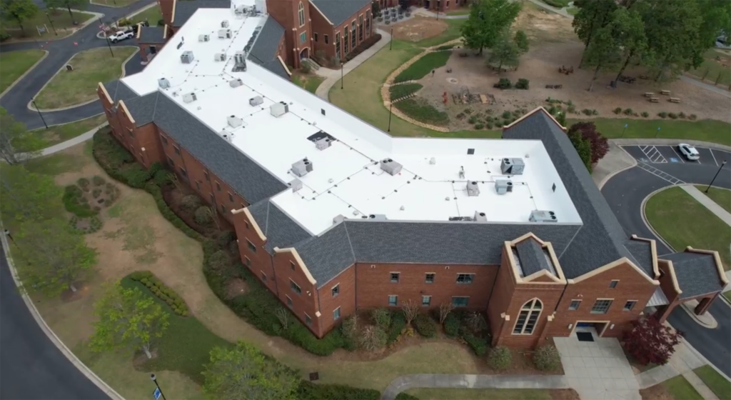 Aerial view of a completed roof replacement on a large brick building with white flat roofing and dark shingle sections by Invictus Roofing