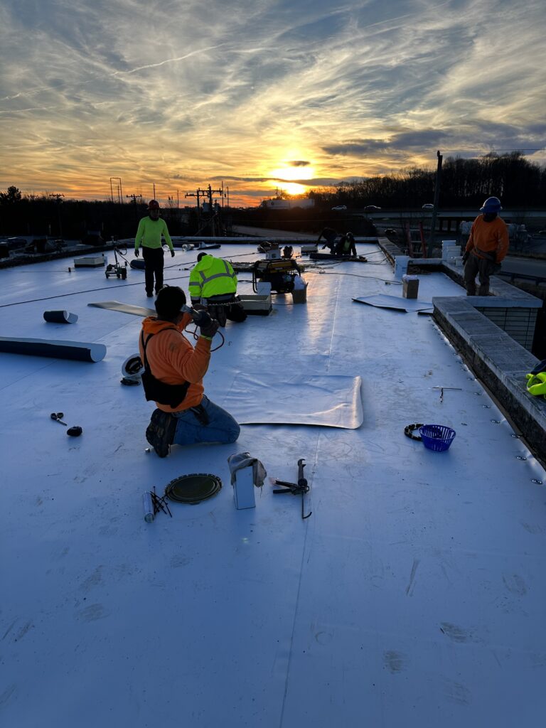 Invictus commercial roofing contractor installing a flat commercial roof for a business property at sunset