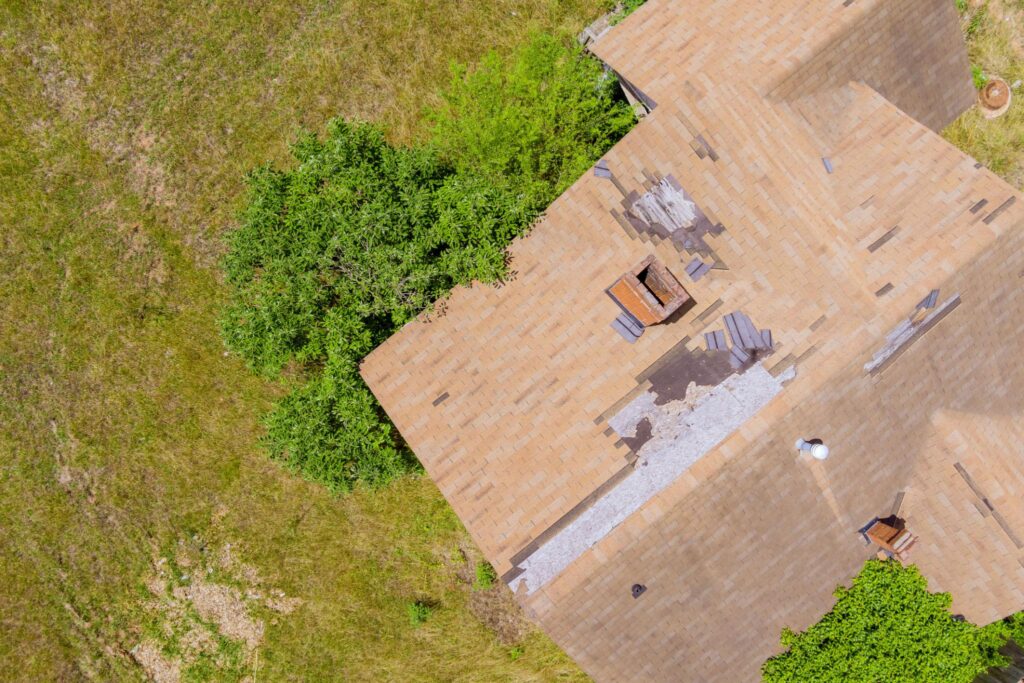 Drone view of a storm-damaged asphalt shingle roof with missing and lifted shingles needing roof shingle repair in Winchester, Georgia.