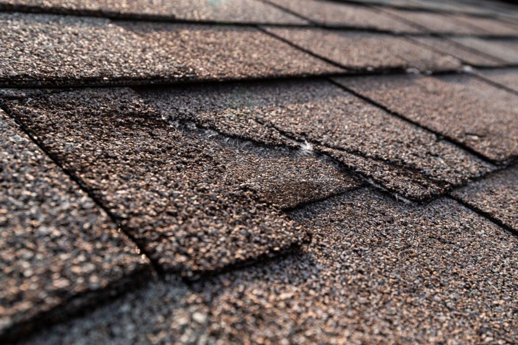 Close-up of damaged asphalt shingles showing lifted and missing tabs needing roof shingle repair in Vickery, Georgia